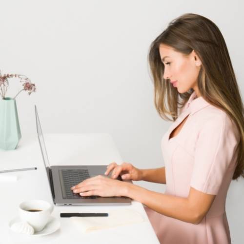 Women typing Conversion Copywriting Tips on a laptop. The women is wearing a pink dress.