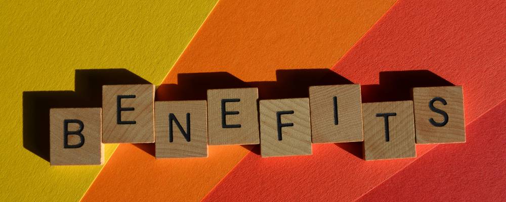 The word benefit is wrriten on small scrabble tiles. The tiles are on a yellow, orange and red background.