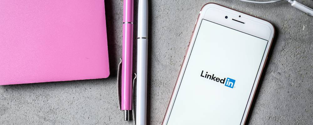 LinkedIn app opening up on an iphone next to a pink and white pen as well as a pink book.
