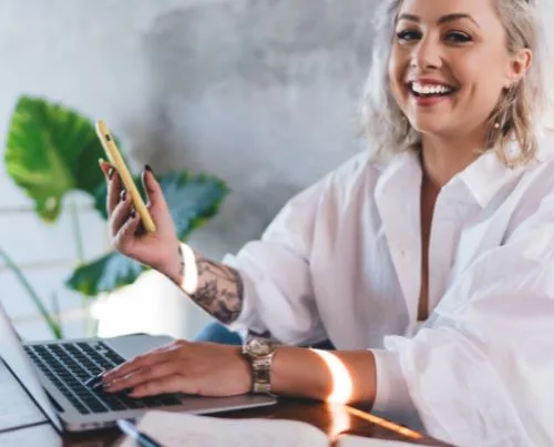 Smiling woman in white shirt reads blog content on her laptop.
